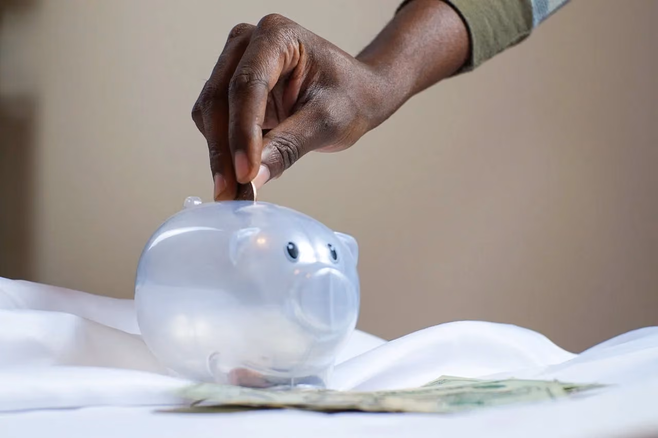 Person dropping a coin into a clear piggy bank, representing smart saving and budget-conscious marketing