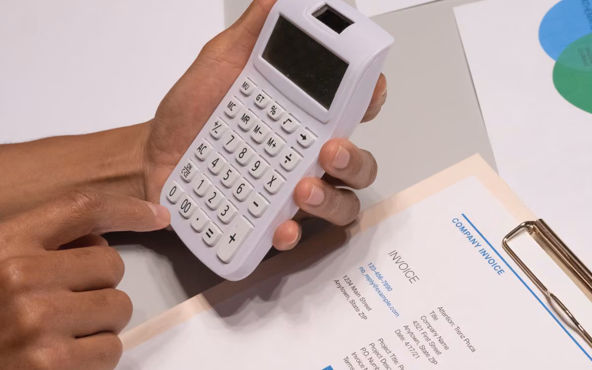 Hands using a calculator next to a printed invoice