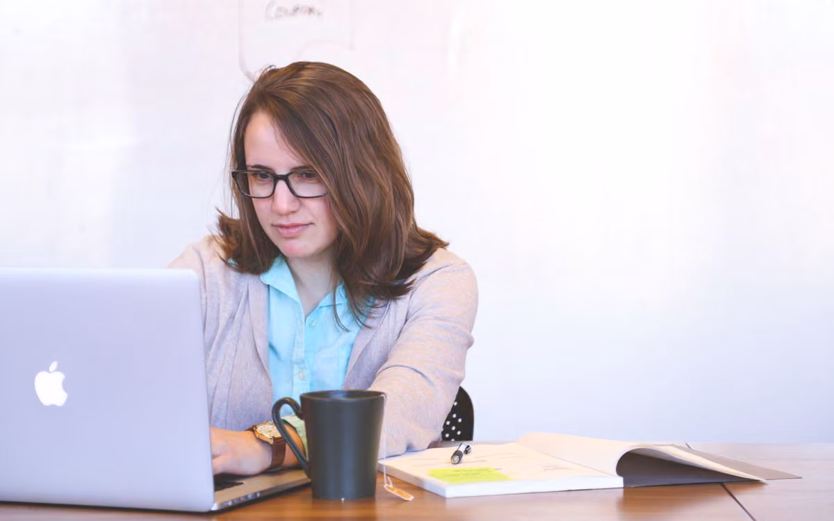 Businesswoman working on a laptop at a desk with a notebook and coffee