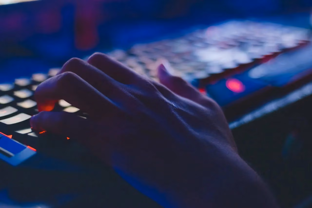 Close-up of hands typing on a computer keyboard with blue and red backlighting