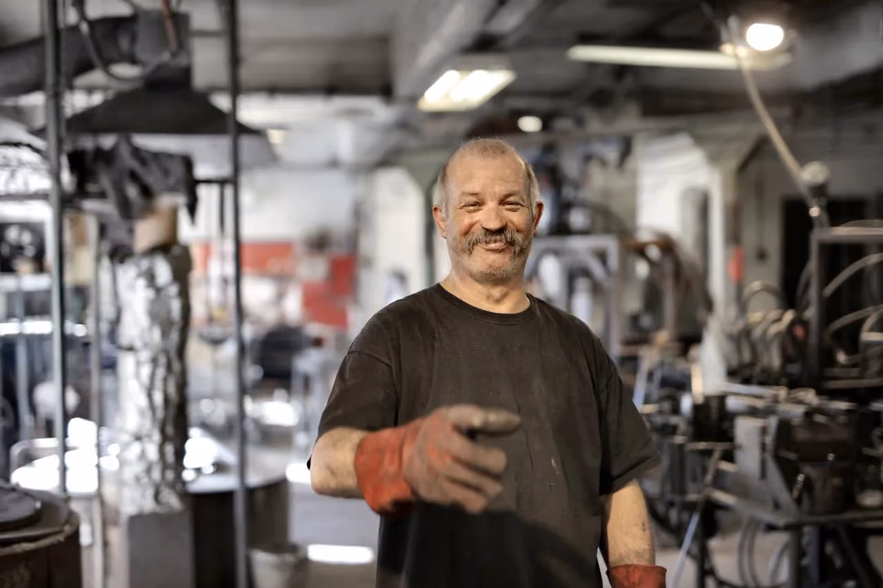 Smiling manufacturing worker wearing gloves on a busy workshop floor