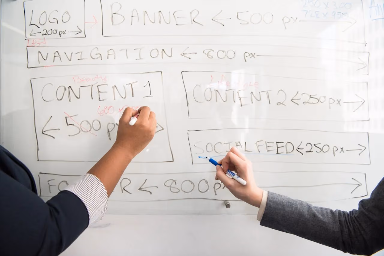 Two colleagues planning strategy together at a whiteboard with coloured markers