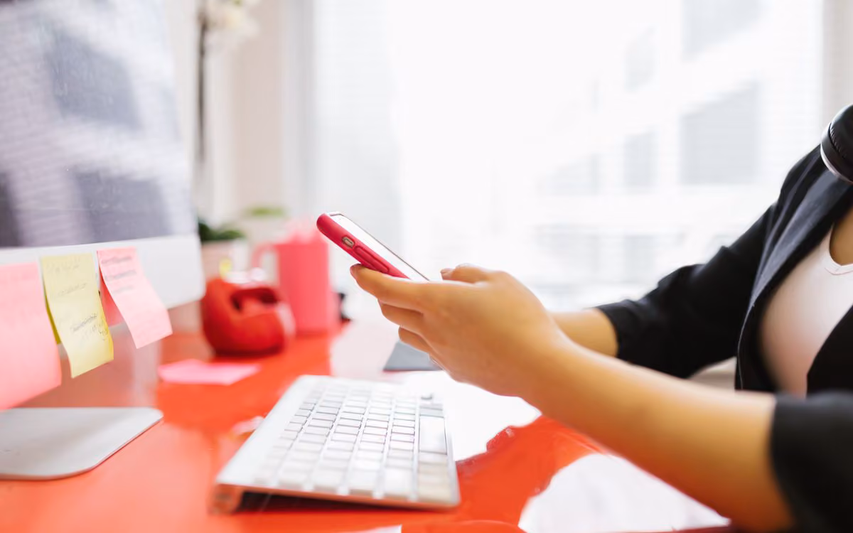 Person checking a smartphone at an office desk beside a keyboard