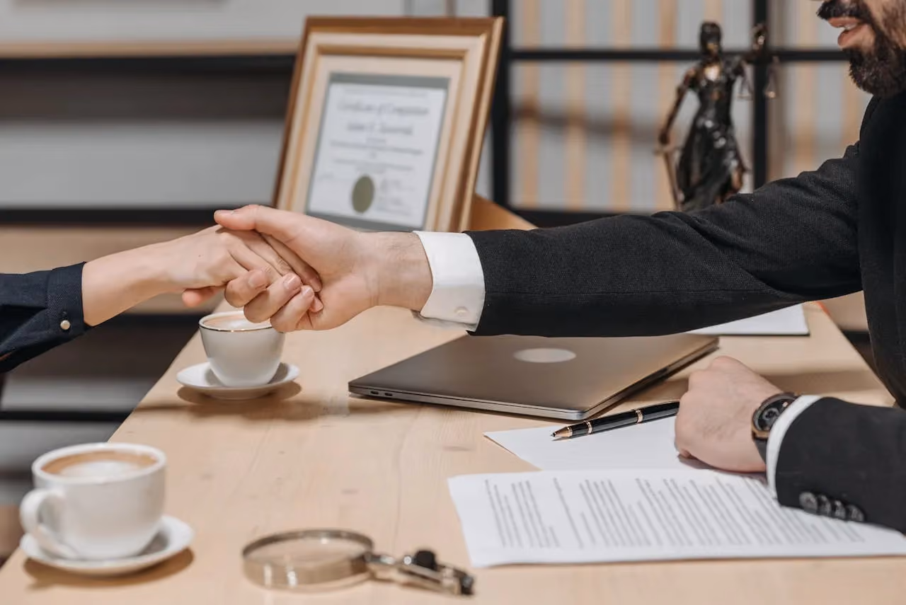 Two professionals shaking hands across a desk after a business agreement