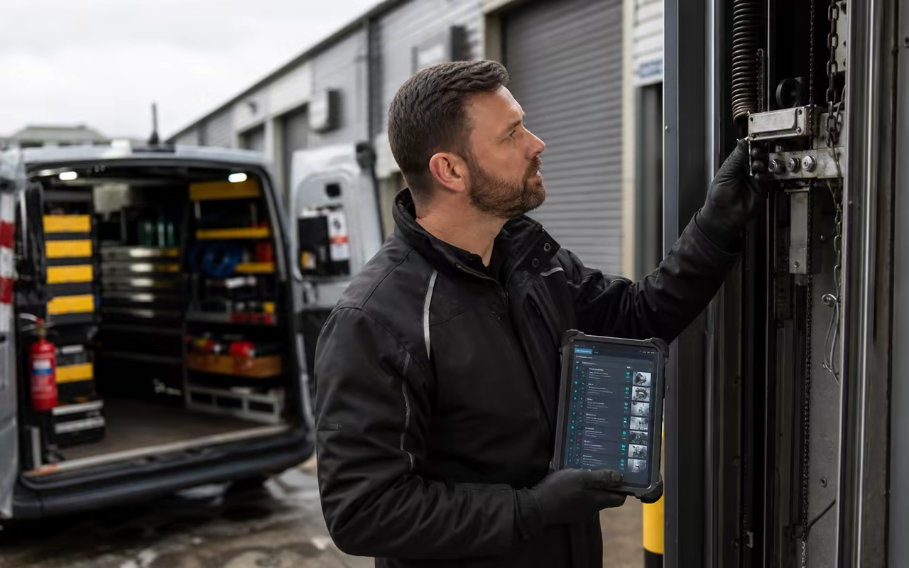 Commercial door engineer checking a mechanism with a tablet beside a stocked service van